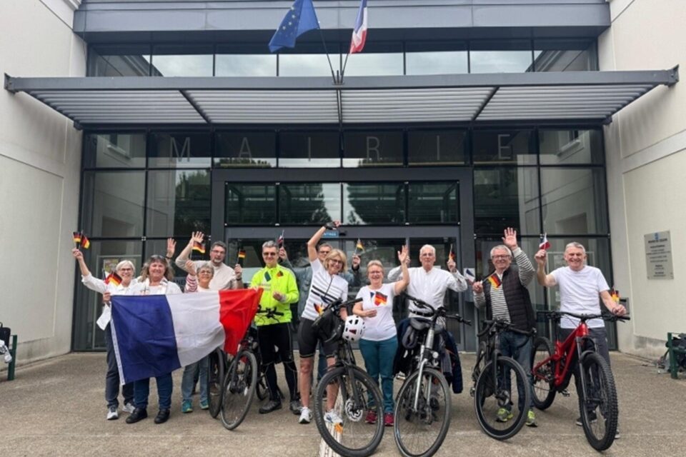 Photo de l'équipe de Cesson sans frontières qui va participer à l'opération Run and Bike. On voit des hommes et des femmes avec des vélos et en tenu de cyclistes ou de coueurs, ainsi qu'un Drapeau Français. Ils sont en face de la mairie de Cesson.
